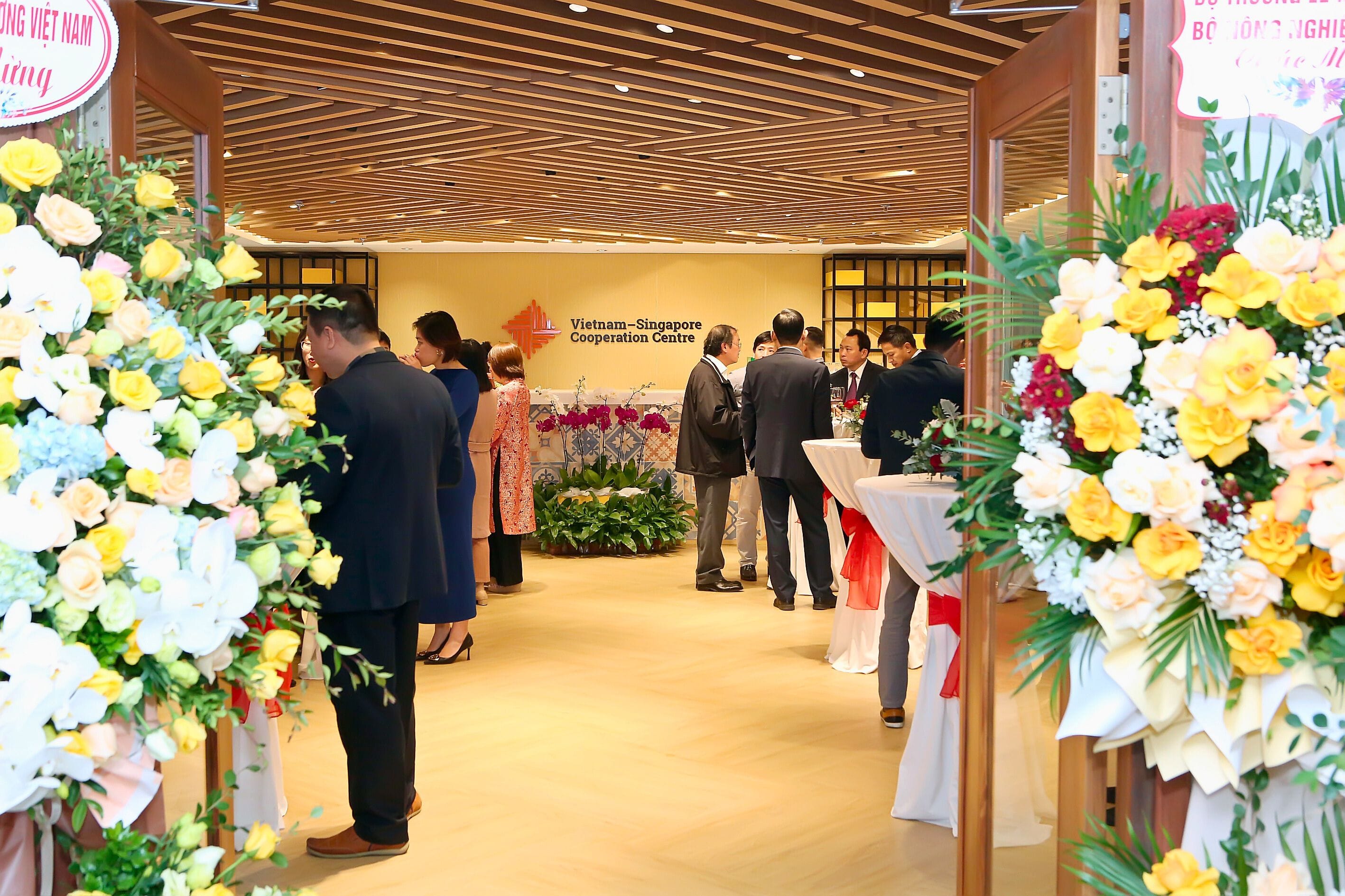 Event entrance framed by flowers, with people gathering at "Vietnam-Singapore Cooperation Centre."